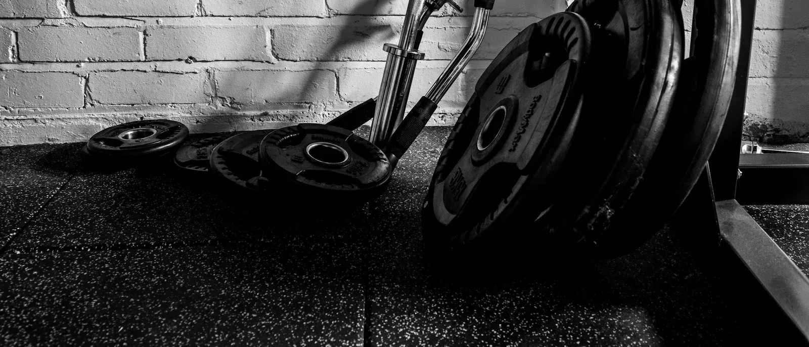 Weight plates and a barbell stacked against a white brick wall in a gym, black and white