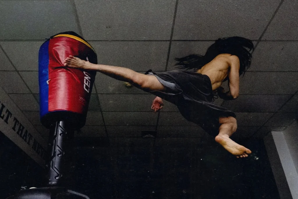 Caleb So throwing a jumping spinning kick at a heavy bag